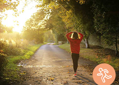 Femme en tenue de sport faisant son jogging dasn une allée boisée et au soleil